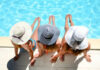 Three people in hats sitting by the pool