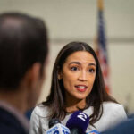 Person speaking to reporters with microphones indoors