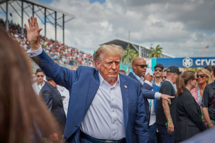 Man in blue suit waving in a crowd outdoors