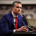 Man in suit sitting at a desk with microphone