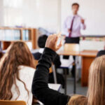 Classroom with student raising hand teacher speaking front