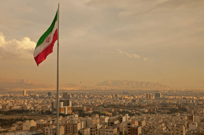 shutterstock_186837098.jpg Iranian flag waving over a city skyline with mountains in the background