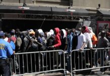 A crowd of people waiting in line outside a venue with a security officer present