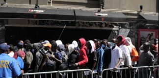 A crowd of people waiting in line outside a venue with a security officer present