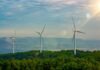 Three wind turbines on a green hillside under a cloudy sky