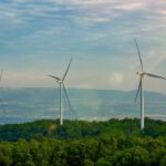 Three wind turbines on a green hillside under a cloudy sky