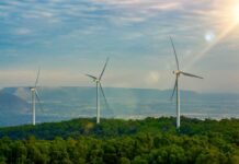 Three wind turbines on a green hillside under a cloudy sky