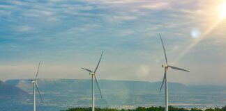 Three wind turbines on a green hillside under a cloudy sky