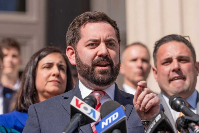 A man in a suit speaking at a press conference with microphones in front of him