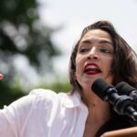A woman passionately speaking at a podium with microphones