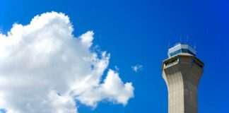 A tall airport control tower against a blue sky with clouds