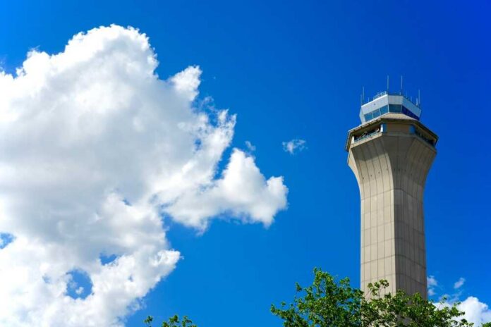 A tall airport control tower against a blue sky with clouds