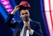 Man in a suit holding a red cap while speaking into a microphone