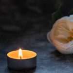 A lit candle beside a white flower on a dark surface