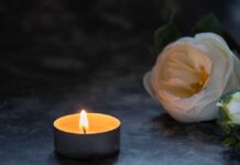 Shocking Loss: Buffy Star Dies Suddenly at 54 A lit candle beside a white flower on a dark surface
