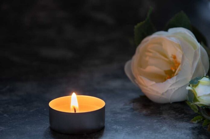 shutterstock_2696086391.jpg A lit candle beside a white flower on a dark surface