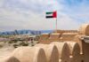 UAE flag waving atop a historic fort with a city skyline in the background