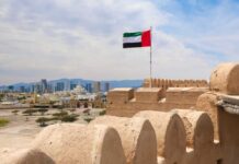Drone Interception Ignites Oil Hub Blaze UAE flag waving atop a historic fort with a city skyline in the background
