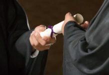 Two individuals exchanging a diploma during a graduation ceremony
