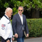 Two men walking outside near green bushes