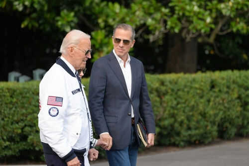 Two men walking outside near green bushes