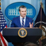 Man speaking at podium with flags in background