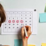 Person marking dates on a calendar with a red marker