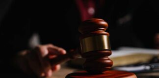 A wooden gavel resting on a table with a blurred hand in the background