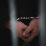 Close-up of handcuffed hands behind bars