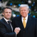 Two political leaders shaking hands in front of a decorated backdrop
