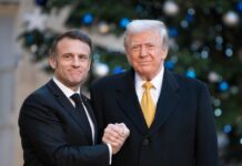 Two political leaders shaking hands in front of a decorated backdrop