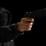 A hooded figure pointing a handgun towards the viewer