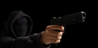 A hooded figure pointing a handgun towards the viewer