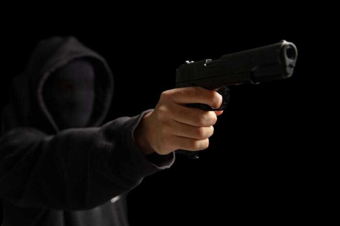 A hooded figure pointing a handgun towards the viewer