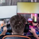 Person wearing headphones at a gaming setup with dual monitors