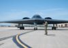 A military personnel stands in front of a B-2 Spirit stealth bomber on an airfield