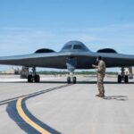 AI Unveils Stealth Bomber Secrets—Real or Hype? A military personnel stands in front of a B-2 Spirit stealth bomber on an airfield