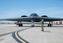 A military personnel stands in front of a B-2 Spirit stealth bomber on an airfield