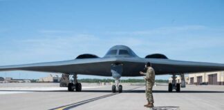 A military personnel stands in front of a B-2 Spirit stealth bomber on an airfield