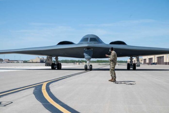 A military personnel stands in front of a B-2 Spirit stealth bomber on an airfield