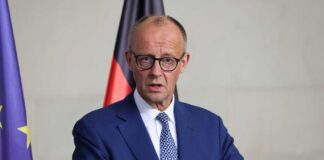 A government official speaking at a press conference with national flags in the background