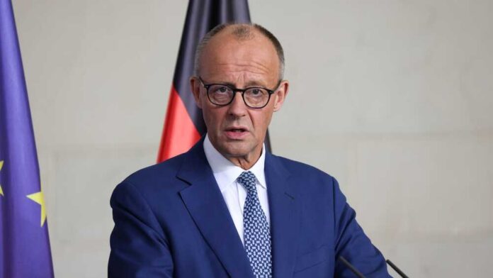 A government official speaking at a press conference with national flags in the background