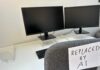 An office desk with two computer monitors and a chair labeled 'REPLACED BY AI'