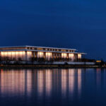 SHOCKING Board Decision: Kennedy Center Goes Dark A modern building illuminated at night beside a calm body of water