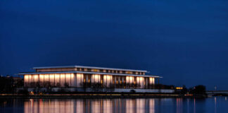 A modern building illuminated at night beside a calm body of water