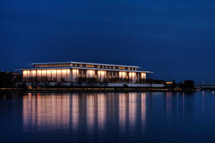 A modern building illuminated at night beside a calm body of water