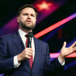 Man in suit speaking with microphone on stage.