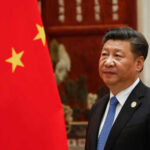 Xi’s War Warning STUNS Trump Crowd Person standing near a Chinese flag indoors