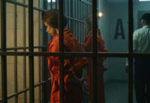 Inmates in orange jumpsuits stand in a jail corridor behind bars
