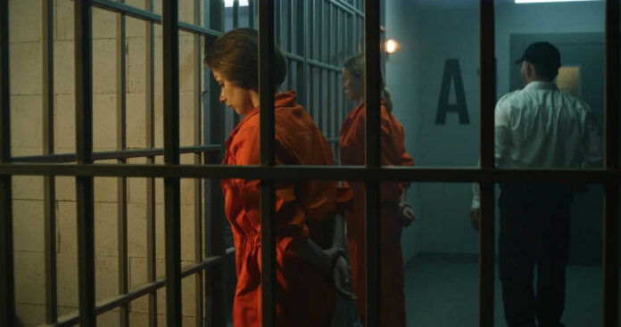 Inmates in orange jumpsuits stand in a jail corridor behind bars
